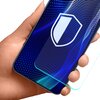 Na zdjęciu widoczna jest dłoń trzymająca telefon z niebieskim ekranem, na którym znajduje się biały symbol tarczy. Obok telefonu unosi się przezroczysta warstwa szkła ochronnego.
