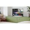 Na zdjęciu znajduje się telewizor SHARP 24HE2745E 24" LED TiVo OS ustawiony na zielonej szafce, z wyświetlonym interfejsem aplikacji streamingowych, takich jak Netflix, YouTube, Disney+, Prime Video, Max i inne. Obok telewizora stoi roślina w doniczce, a 