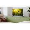 Telewizor SHARP 24HE2745E 24" LED TiVo OS stoi na zielonej szafce, wyświetlając obraz ptaka siedzącego na gałęzi wśród liści. Obok telewizora znajduje się roślina w doniczce.