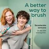 Na zdjęciu widoczna jest osoba trzymająca turkusową szczoteczkę soniczną, obok której znajduje się tekst: "A better way to brush" oraz "Szczoteczka soniczna Do 80 000 wibracji/min." w jasnym, zielonym otoczeniu.
