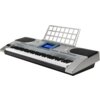 Srebrny keyboard z wyświetlaczem i licznymi przyciskami funkcyjnymi, posiada stojak na nuty oraz dwa duże głośniki po bokach. Na wyświetlaczu widoczny jest niebieski ekran z czarnym tekstem.