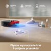 Czarny robot sprzątający znajduje się na granicy drewnianej podłogi i dywanu, z widocznym tekstem "Zwiększenie mocy ssania na dywanach" oraz wykresem z niebieskim i czerwonym wentylatorem. Na dole obrazu widnieje napis "Ultradźwiękowe wykrywanie dywanów".