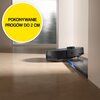 Czarny robot sprzątający pokonuje próg o wysokości 2 cm, co jest oznaczone na podłodze. Na żółtym tle widnieje napis: "POKONYWANIE PRÓGÓW DO 2 CM".