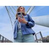 Osoba trzymająca smartfon z widocznym logo "G" na tle konstrukcji architektonicznej z metalowych belek. Ubrana jest w niebieską kurtkę i jasne dżinsy, a na nadgarstku ma zegarek.