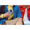 Osoba trzyma w ręku szary smartfon z widocznym logo w kształcie litery "G". Ubrana jest w żółty sweter i niebieską dżinsową kurtkę, siedząc obok osoby w czerwonej kurtce.