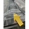 Przezroczysta plastikowa część urządzenia z widoczną żółtą strzałką skierowaną w górę. W tle znajduje się fragment instrukcji lub opakowania z nieczytelnym tekstem.