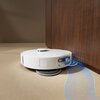 Na zdjęciu widoczny jest spód robota sprzątającego z białą obudową. Robot wyposażony jest w dwie okrągłe szczotki czyszczące oraz wirującą szczotkę boczną.