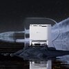 Na zdjęciu znajduje się robot sprzątający z widocznym logo "EZVIZ" na jego powierzchni. Wokół robota rozmieszczone są różne przedmioty, takie jak waga, okrągła pufa, para kapci oraz fragment kanapy, a niebieskie linie sugerują jego trasę sprzątania.