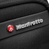 Zbliżenie na czarną walizkę z widocznym logo "Manfrotto" w srebrnym kolorze oraz czerwonym okrągłym symbolem obok. Powierzchnia walizki ma teksturę z drobnymi wypustkami, co nadaje jej elegancki wygląd.