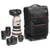 Czarna walizka z logo "Manfrotto" na górnej kieszeni, z czerwonymi akcentami i solidnymi kółkami, stoi obok zestawu sprzętu fotograficznego, w tym kilku aparatów i obiektywów. Walizka ma kilka zamykanych na zamek kieszeni i paski zabezpieczające.