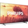 Telewizor z dużym ekranem wyświetla obraz przedstawiający miasto z wieżowcami, nad którym unosi się duża postać przypominająca potwora oraz dwa helikoptery na tle pomarańczowego nieba. Na środku ekranu widnieje duży, biały napis "PHILIPS".