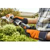 Na zdjęciu widoczne są akumulatorowe nożyce do żywopłotu w kolorze pomarańczowo-czarnym z białymi akcentami. Na obudowie znajduje się logo "STIHL" oraz kilka symboli ostrzegawczych.