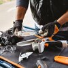 Na zdjęciu widoczna jest piła akumulatorowa z napisem "STIHL" na prowadnicy, trzymana przez osobę w rękawicach roboczych. Obok piły znajdują się okulary ochronne, ładowarka oraz osłona prowadnicy.