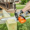 Na zdjęciu widać osobę używającą pomarańczowej piły łańcuchowej do cięcia drewnianej belki. Na obudowie piły widoczny jest napis "STIHL MSE 141C", a na prowadnicy piły znajduje się logo "STIHL".