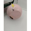 Różowy kettlebell z widocznymi śladami rdzy i odpryskami farby na powierzchni, z żółtą strzałką wskazującą na uszkodzenie. Produkt znajduje się na białej powierzchni obok ciemnozielonego elementu.