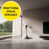 W nowoczesnym, minimalistycznym wnętrzu przy ścianie stoi odkurzacz na stacji dokującej. W lewym górnym rogu znajduje się żółte koło z napisem "PRAKTYCZNA STACJA DOKUJĄCA".