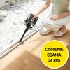 Osoba używa odkurzacza ręcznego do czyszczenia szczeliny przy podłodze, a na zdjęciu widoczny jest żółty okrąg z napisem "CIŚNIENIE SSANIA 24 kPa". Podłoga jest drewniana, a w tle widać fragment powierzchni z płytek.