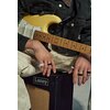 Na zdjęciu widoczna jest gitara elektryczna trzymana przez osobę, której dłonie spoczywają na wzmacniaczu z logo "Laney". Na palcach osoby znajdują się białe i czarne pierścienie.