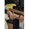 Na zdjęciu widać osobę siedzącą na wzmacniaczu marki Laney, trzymającą gitarę elektryczną w kolorze kremowym. Na palcach widoczne są czarne i białe pierścienie.