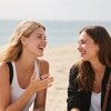 Na zdjęciu widać dwie osoby siedzące na plaży, uśmiechające się do siebie. Jedna z nich ma na palcu czarny pierścień.