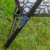 Na zdjęciu widoczny jest fragment metalowej ramy fotela ogrodowego z mechanizmem regulacji, ustawiony na trawie. Siedzisko fotela pokryte jest materiałem w szaro-żółty wzór liści.