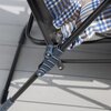 Na zdjęciu widoczny jest fragment metalowej konstrukcji fotela ogrodowego z mechanizmem składania oraz materiał w kratę w odcieniach niebieskiego, brązowego i białego. Tło stanowi jasna, drewniana podłoga tarasowa.
