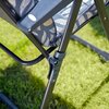 Na zdjęciu widoczny jest fragment metalowej konstrukcji fotela ogrodowego z wzorzystą poduszką w odcieniach niebieskiego i białego, ustawionego na trawie. Konstrukcja fotela ma ciemny kolor, a na jednym z elementów znajduje się mała, okrągła plakietka.