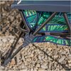 Fragment leżaka ogrodowego z metalową ramą i materiałem w zielone liście na tle kamieni. Na ramie widoczny jest mechanizm składania.