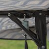 Zbliżenie na metalowy stelaż huśtawki ogrodowej z widoczną sprężyną i śrubami mocującymi. W tle znajduje się materiał z wzorem w liście w odcieniach szarości i beżu.