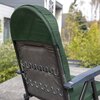 Na zdjęciu widoczny jest tył ogrodowego fotela z zielonym materiałowym obiciem i metalową ramą, ustawiony na zewnątrz na tle roślinności i budynku. Fotel ma ciemne podłokietniki i widoczne sprężyny w oparciu.