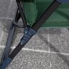 Zbliżenie na fragment konstrukcji fotela ogrodowego z zielonym materiałem i metalowym stelażem w ciemnym kolorze, ustawionego na szarej, kamiennej powierzchni. Widoczne są detale łączenia elementów stelaża.