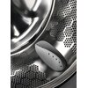 Zbliżenie na wnętrze bębna pralki z widocznymi otworami i plastikowym elementem w środku. Powierzchnia bębna jest metaliczna i błyszcząca.