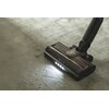 Odkurzacz z widocznym logo "Hoover" i napisem "anti-twist" na głowicy, odkurza dywan z rozsypanymi okruchami. Głowica odkurzacza jest wyposażona w oświetlenie LED.