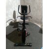 Na zdjęciu widoczny jest rower magnetyczny z czarną ramą i pedałami, ustawiony na szarej powierzchni. Rower posiada kierownicę z uchwytami oraz siedzisko, a w tle widać szarą ścianę.