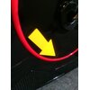 Czarne tło z czerwonym okręgiem, na którym znajduje się żółta strzałka skierowana w dół. W tle widoczna jest część mechanizmu roweru magnetycznego.