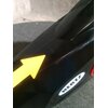 Czarny element roweru magnetycznego z żółtą strzałką skierowaną w górę oraz widocznym logo "HERTZ" na białym tle. Tło jest szare i teksturowane.