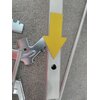 Na zdjęciu widoczny jest fragment metalowej konstrukcji z żółtą strzałką wskazującą na otwór w metalowym profilu. Obok znajdują się elementy metalowe o nieregularnych kształtach, leżące na szarej powierzchni.