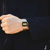 Na zdjęciu widoczny jest zegarek cyfrowy na srebrnej bransolecie, noszony na nadgarstku osoby ubranej w ciemną odzież. Na tarczy zegarka widnieje napis "CASIO" oraz cyfrowy wyświetlacz pokazujący godzinę 19:52:21 i datę 5-2.