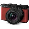 Czerwony aparat bezlusterkowy z czarnymi elementami, na którym widoczne jest logo "LUMIX". Obiektyw ma oznaczenia "S 1:4.5-6.3 / 18-40mm ⌀62".