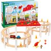Na zdjęciu znajduje się zestaw kolejki BRIO World Mega Spiral Set 63611400, składający się z drewnianych torów na białych podporach, czerwonego mostu, helikoptera, samochodów strażackich oraz figurek. W tle widoczne jest opakowanie z grafiką przedstawiają