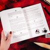 Otwarta książka z widocznym tekstem, w tym fragmenty oznaczone numerami paragrafów: §40, §41, §42, §43. Na stronie znajduje się ilustracja wilka oraz rysunek pająka, a w tle widoczna jest czerwona powierzchnia i kilka rekwizytów, w tym ołówek i kostka do 