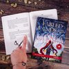 Na zdjęciu widać otwartą książkę z tekstem, obok której leży książka "Fabled Lands: Rozdarte Królestwo" autorstwa Dave'a Morrisa i Jamie'ego Thomsona. Na okładce książki znajduje się ilustracja postaci w czerwonym płaszczu na tle zamku, a na dole widnieje