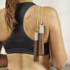 Na zdjęciu widoczna jest osoba w sportowym topie, trzymająca skakankę z drewnianymi rączkami, na których znajduje się napis "HOT by Kettler". Skakanka ma jasnozielony sznurek.