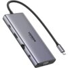 Na zdjęciu widoczny jest hub USB typu C w metalicznej obudowie z kilkoma portami, w tym HDMI, Ethernet i VGA, oraz z krótkim kablem zakończonym wtykiem USB-C. Na obudowie znajduje się logo "UGREEN 4K 60Hz".