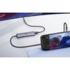 Na zdjęciu widoczny jest hub UGREEN CM511 6w1 USB Typu C, pasywny, podłączony do urządzenia przenośnego z wyświetlaczem pokazującym grę wyścigową. Hub ma kilka portów i jest połączony z monitorem za pomocą kabla.