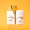 Na zdjęciu widoczne są dwa opakowania produktu "BESTLAB BEST ELECTROLYTES" na tle pomarańczowej ściany, z kwiatem umieszczonym pomiędzy nimi. Na opakowaniach znajdują się informacje o składnikach: "Mg", "Na", oraz ikony wskazujące, że produkt jest wegańsk