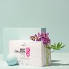 Pudełko produktu "BESTLAB BestCollagen" z napisem "Collagen peptides, Vitamins A, C, E, MSM" stoi na tle jasnoniebieskiej ściany, obok niego znajduje się fioletowy kwiat i niebieska kula. Na pudełku widoczne są również ikony suplementu diety oraz masa net