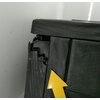 Na zdjęciu widoczny jest fragment grafitowej skrzyni ogrodowej z uszkodzeniem w postaci pęknięcia na krawędzi. Na powierzchni skrzyni znajduje się żółta strzałka wskazująca na uszkodzenie.