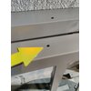Na zdjęciu widoczny jest fragment metalowej konstrukcji z dwoma otworami oraz żółtą strzałką wskazującą na jeden z otworów. Tło jest szare i teksturowane.