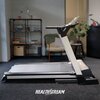 Bieżnia elektryczna znajduje się w pomieszczeniu z dywanem, w tle widać regał z książkami, fotel oraz rośliny. Na dole zdjęcia widoczny jest napis "HEALTHSTREAM".